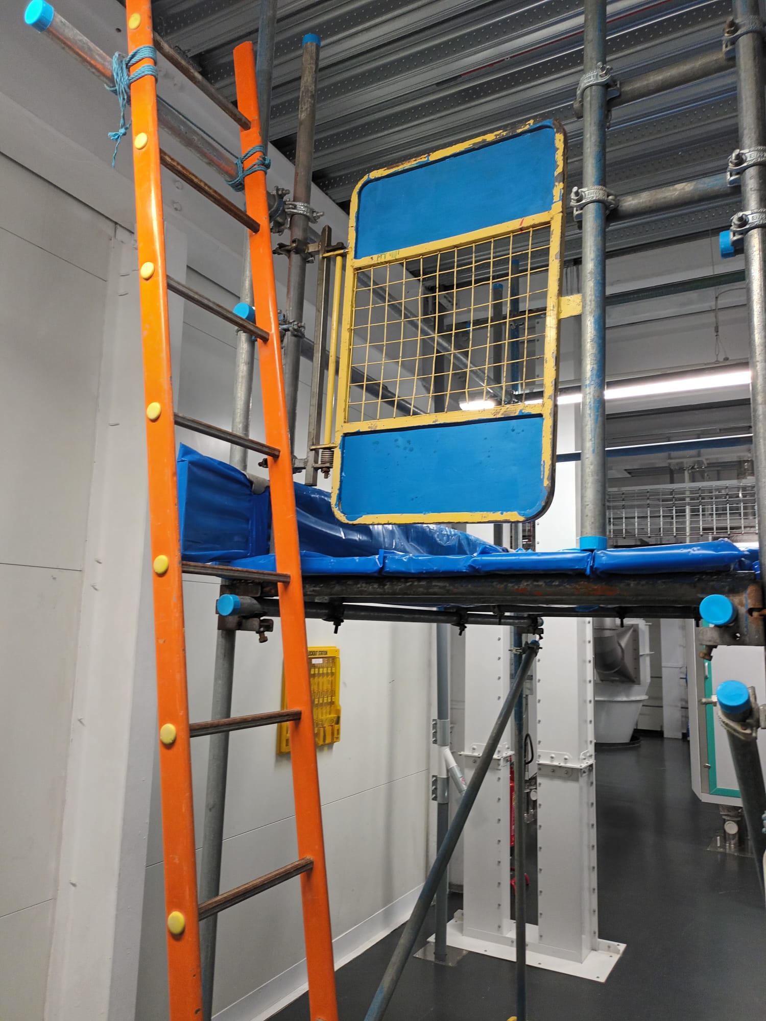 Industrial scaffolding with ladder access and safety gate inside a factory building